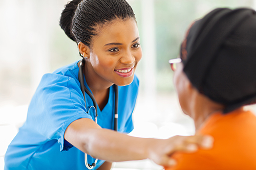 Nurse leaning over to place a hand on a resident's shoulder smiling